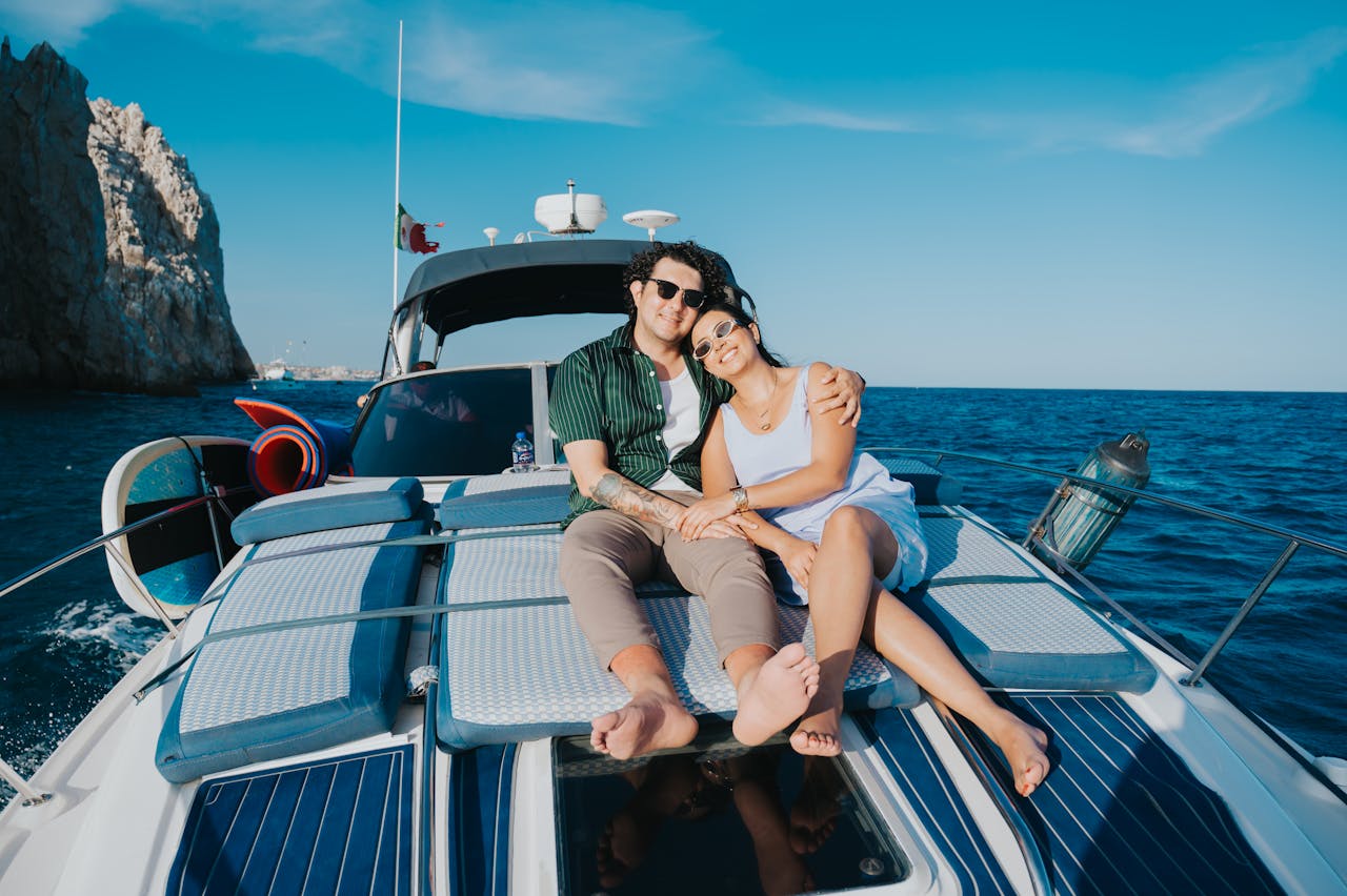 services-02 A couple enjoying a sunny day on a yacht with the ocean and cliffs in the background.