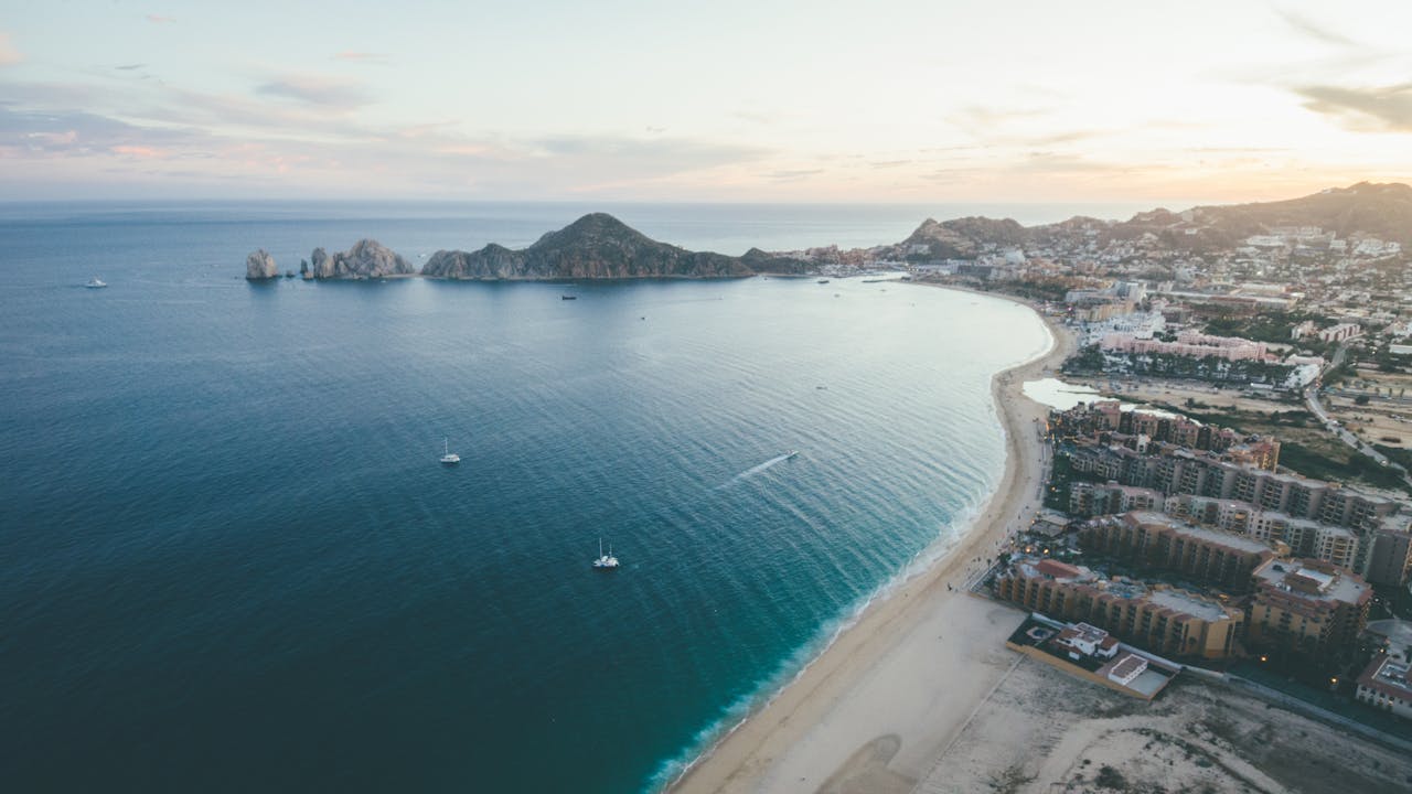 services-03 A stunning aerial view of Cabo San Lucas coastline during sunset, showcasing the beautiful seascape and cityscape.